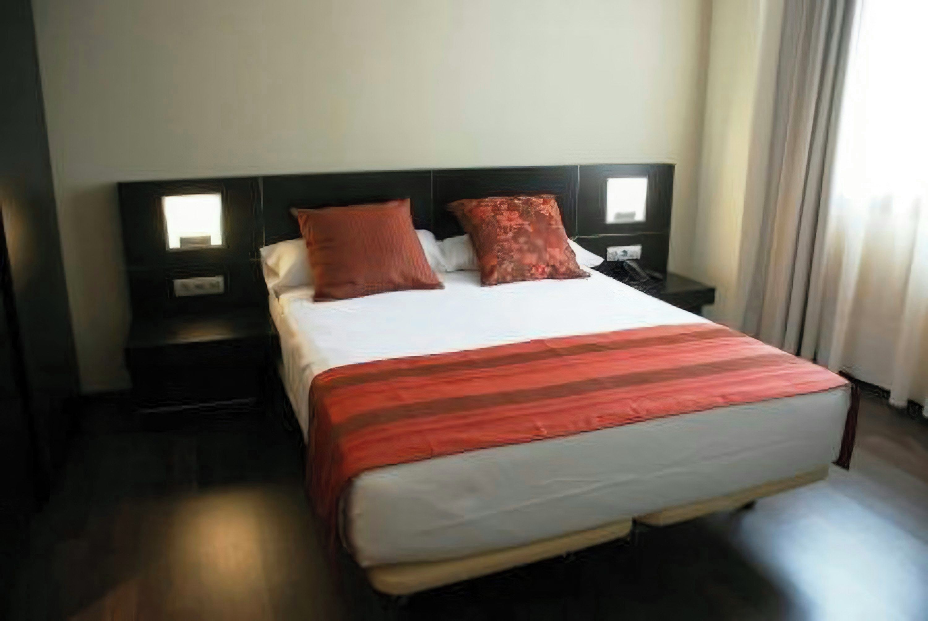 Una habitación de hotel con una cama grande, dos mesitas de noche y un ventanal con cortinas.