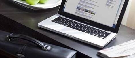 Una computadora portátil sobre un escritorio, junto con un plato de manzanas verdes y un periódico.