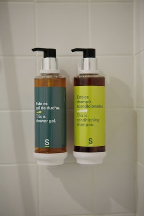 Two bottles of shower gel and conditioning shampoo on a tiled wall. - Sercotel Aura Algeciras (Algeciras)