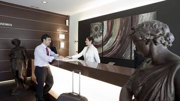 Zona de recepción con una recepcionista, un huésped y una estatua.