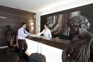 A reception area with a receptionist, a guest, and a statue. - Sercotel Aura Algeciras (Algeciras)