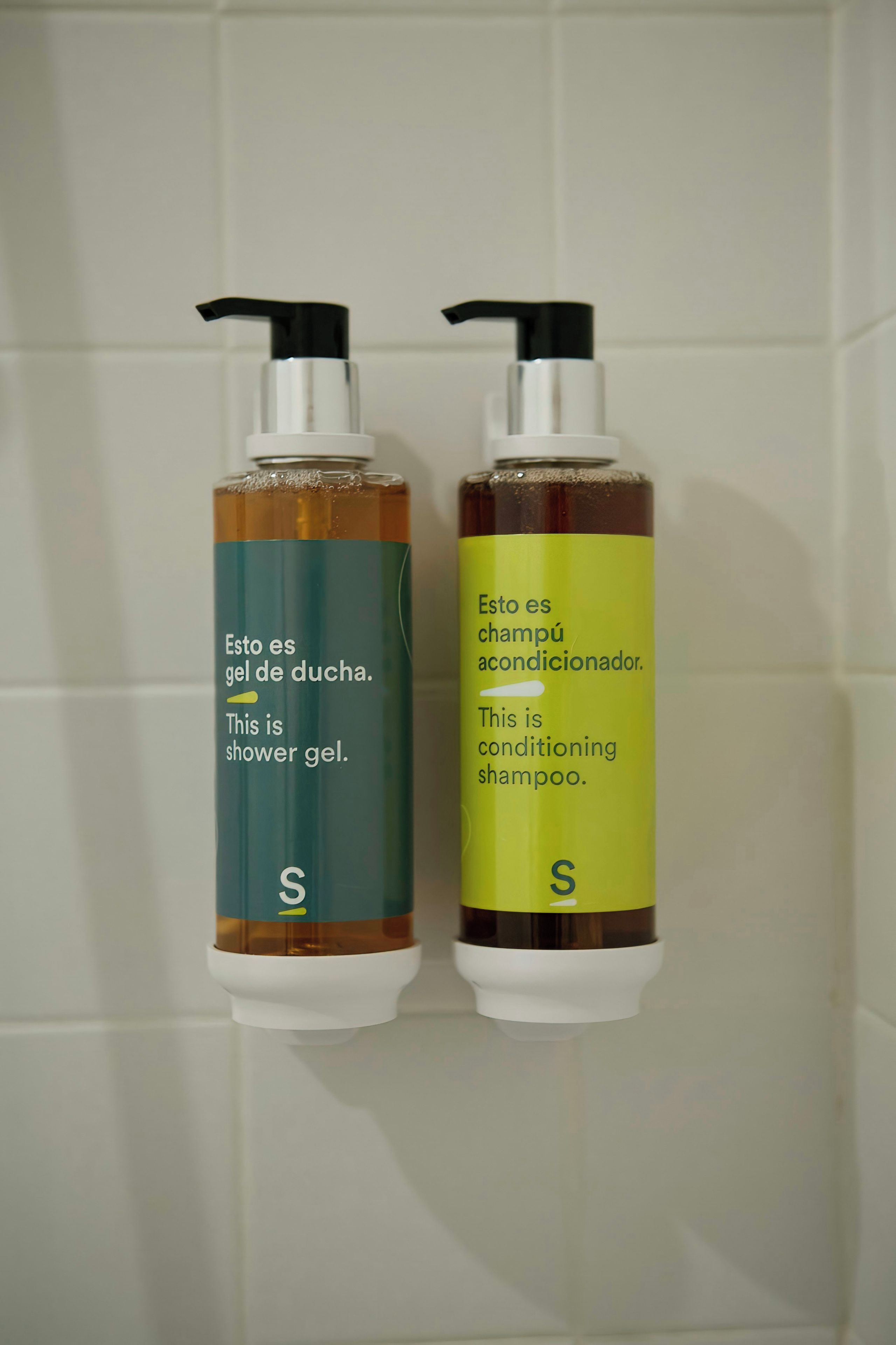 Two bottles of shampoo and shower gel on a tiled wall.