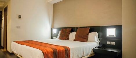 A hotel room with a large bed, a nightstand, a wall-mounted lamp, and a power outlet.