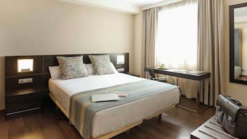 A hotel room with a bed, bedside tables, a desk, a chair, a suitcase, and a large window with curtains.