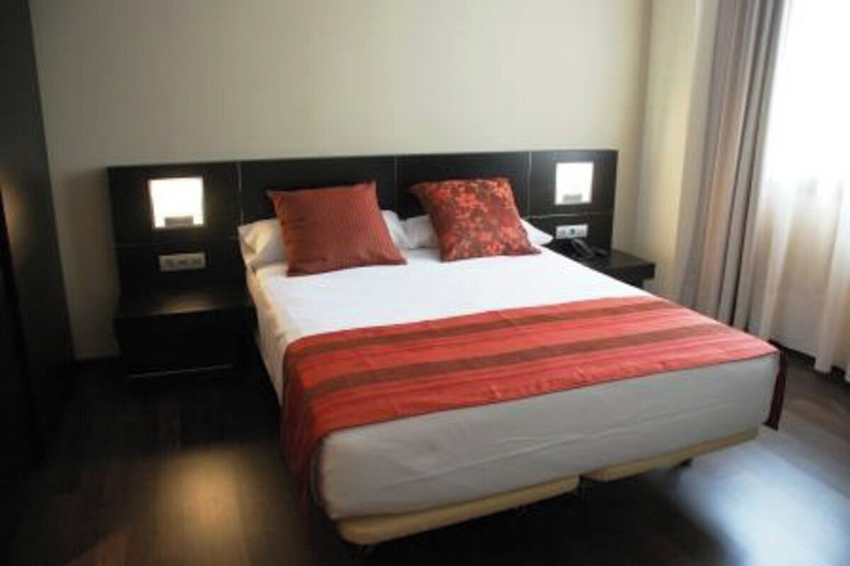 A hotel room with a bed, two nightstands, and a window with curtains.