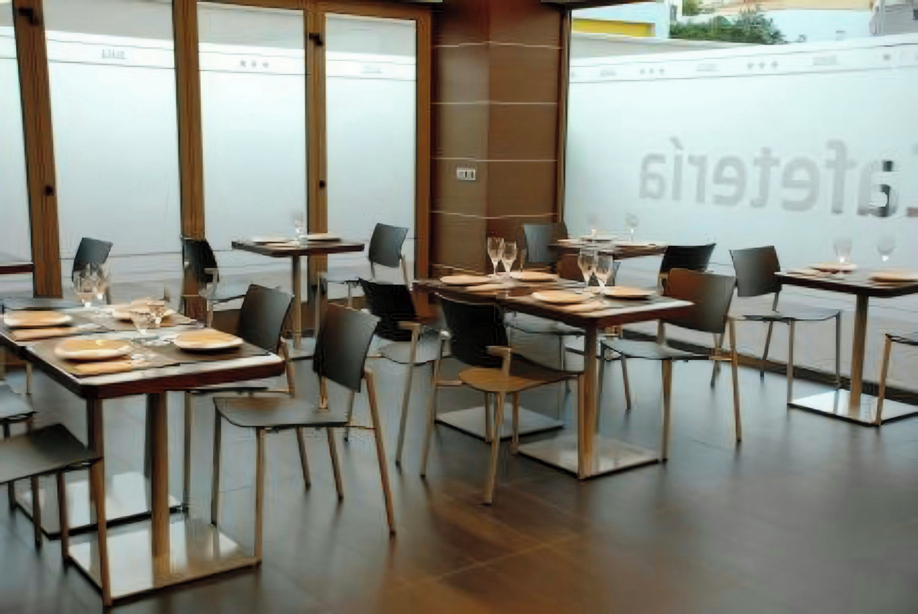 A restaurant interior with tables set for dining, chairs, and a large window with frosted glass.