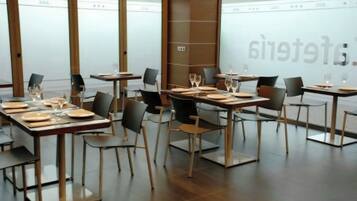 Interior de restaurante con mesas dispuestas para comer, sillas y un gran ventanal con vidrio esmerilado.