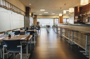 Un restaurante espacioso con mesas y sillas altas, una zona de bar y vistas amplias a través de los grandes ventanales.