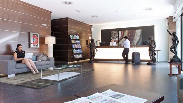 A modern hotel lobby with a reception desk, seating area, and a statue. - Sercotel Aura Algeciras (Algeciras)
