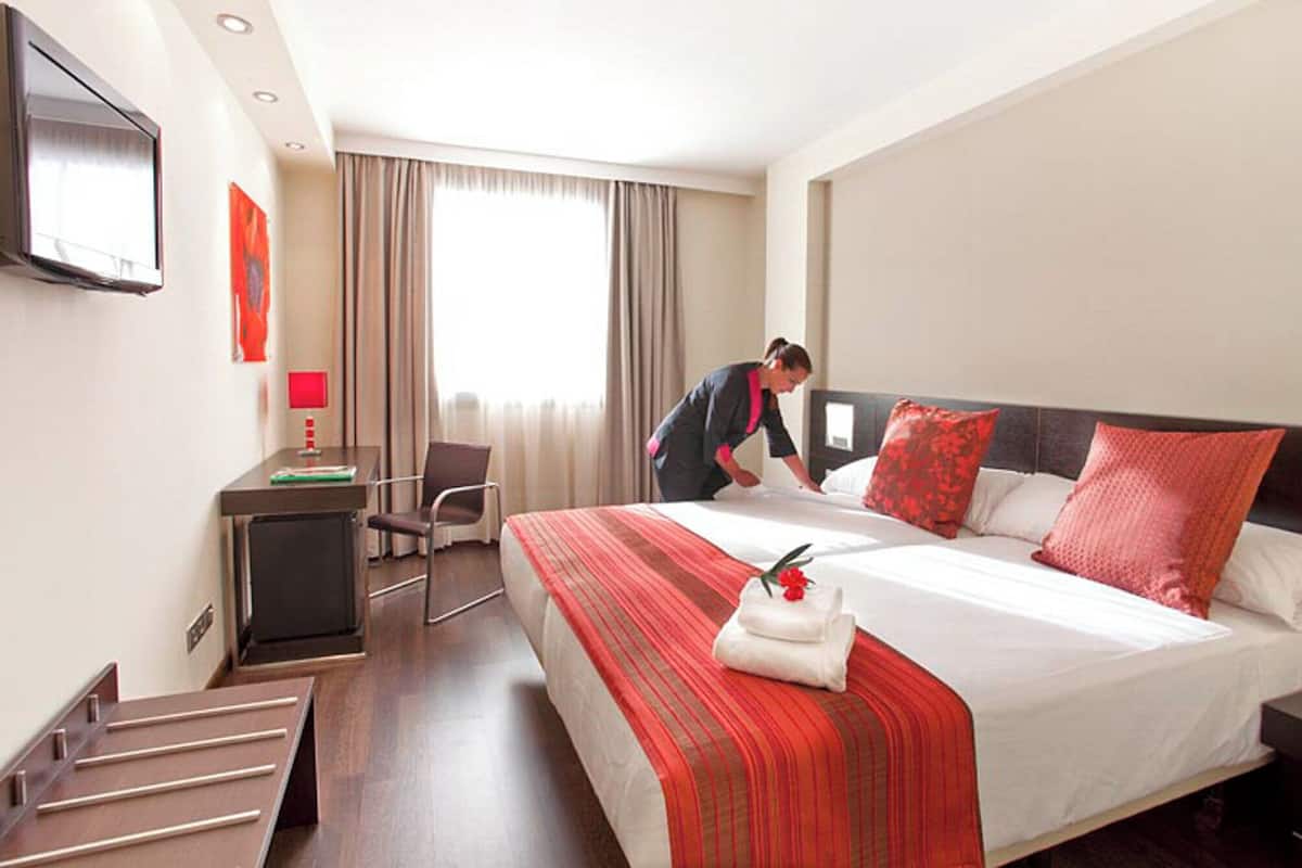 A hotel room with a bed, a desk, a chair, a TV, and a window with curtains.