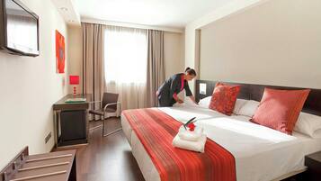 Habitación de hotel con cama, escritorio, silla y televisión en la pared.