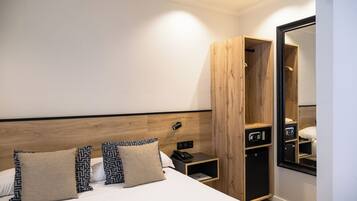 A modern hotel room with a large bed, a wooden wardrobe, a bedside table with a phone, and a mirror.