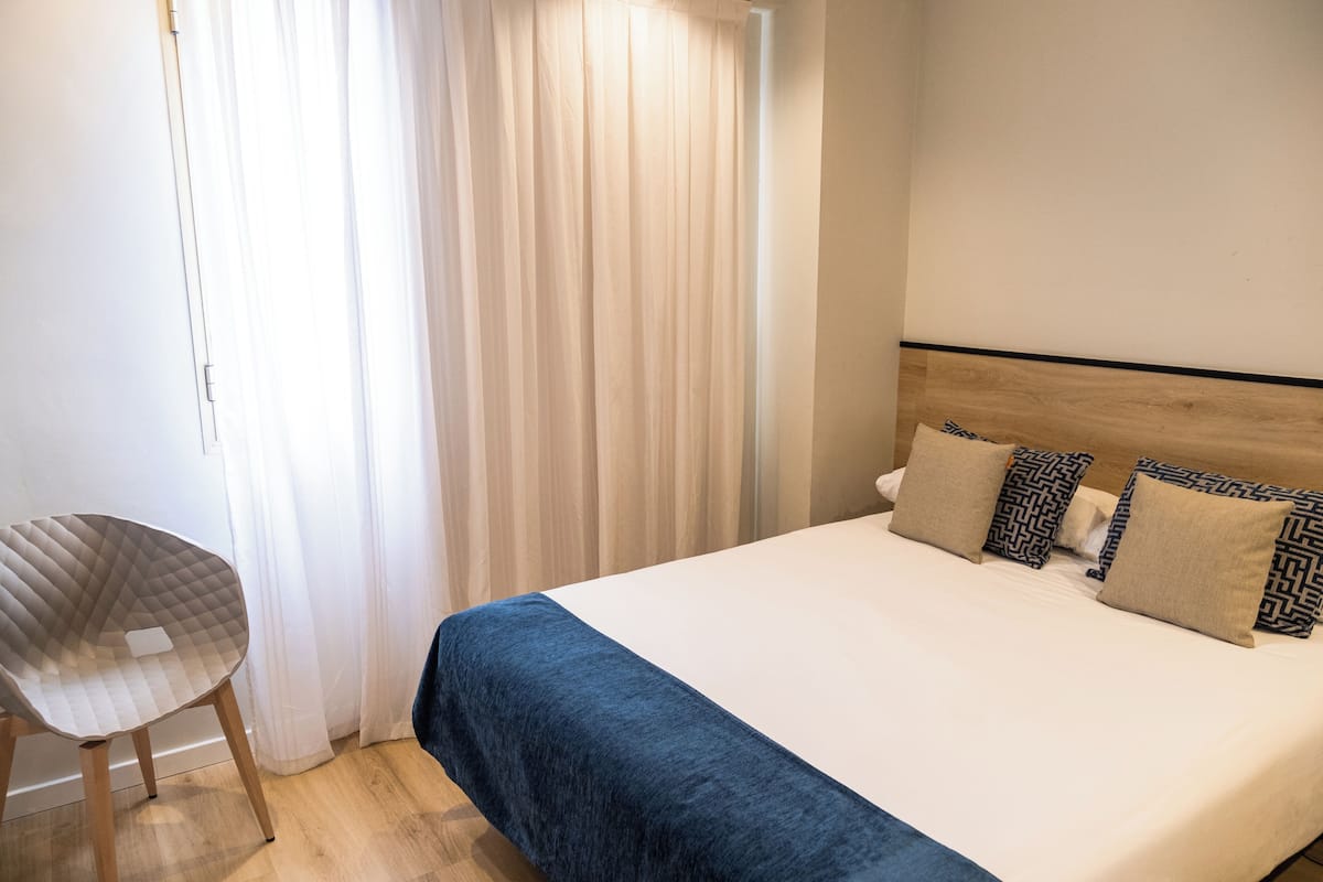 Hotellihuone, jossa on sänky, tuoli ja ikkuna, jossa on verhot.