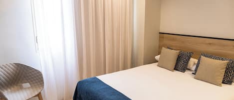 A hotel room with a bed, a chair, and a window with curtains.
