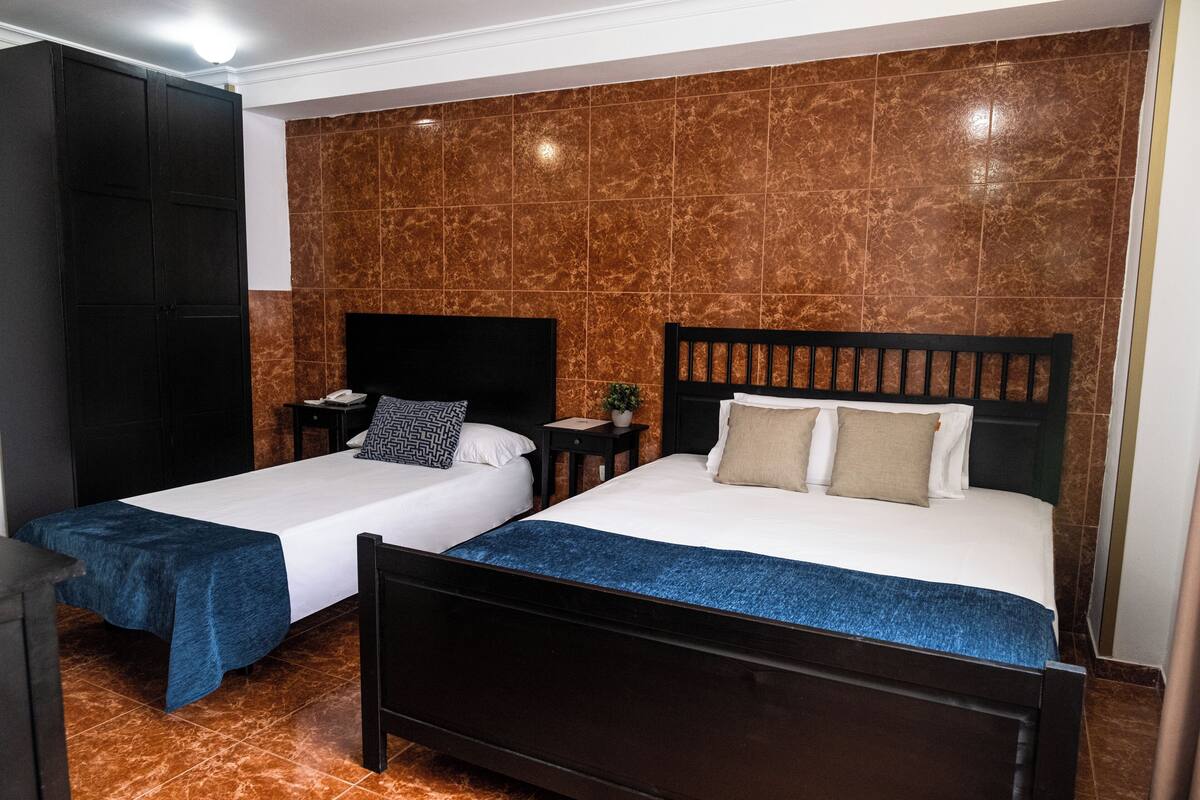 Hotellihuone, jossa on kaksi sänkyä, vaatekaappi ja pieni pöytä, jonka päällä on kasvi.