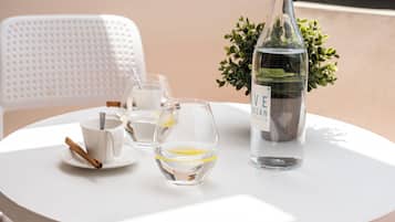 A round table with a white tablecloth, a glass bottle, two glasses, and a white mug with a cinnamon stick.