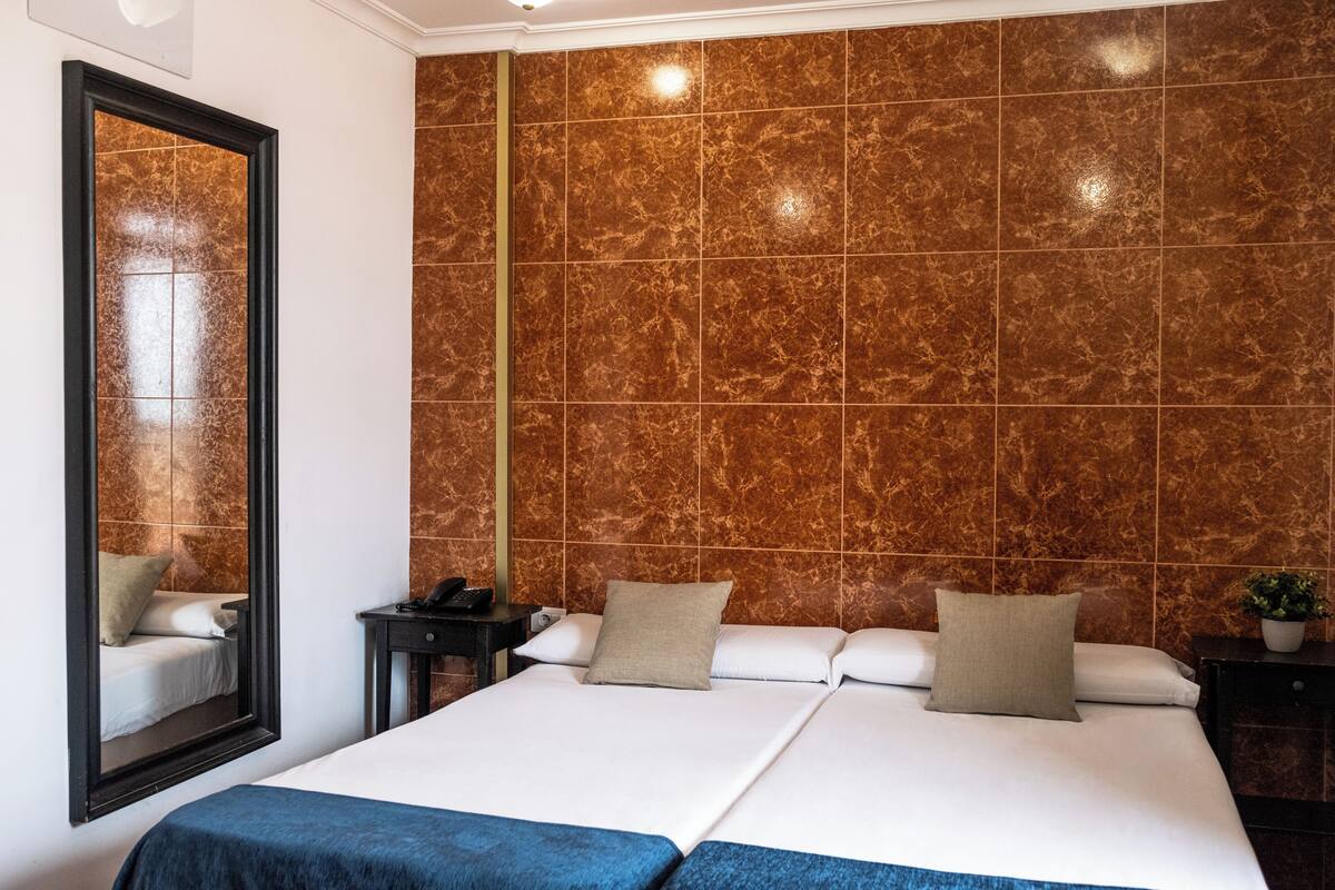 Hotellihuone, jossa on suuri sänky, yöpöytä, peili ja seinä, jossa on marmorikuvioitu pinta.