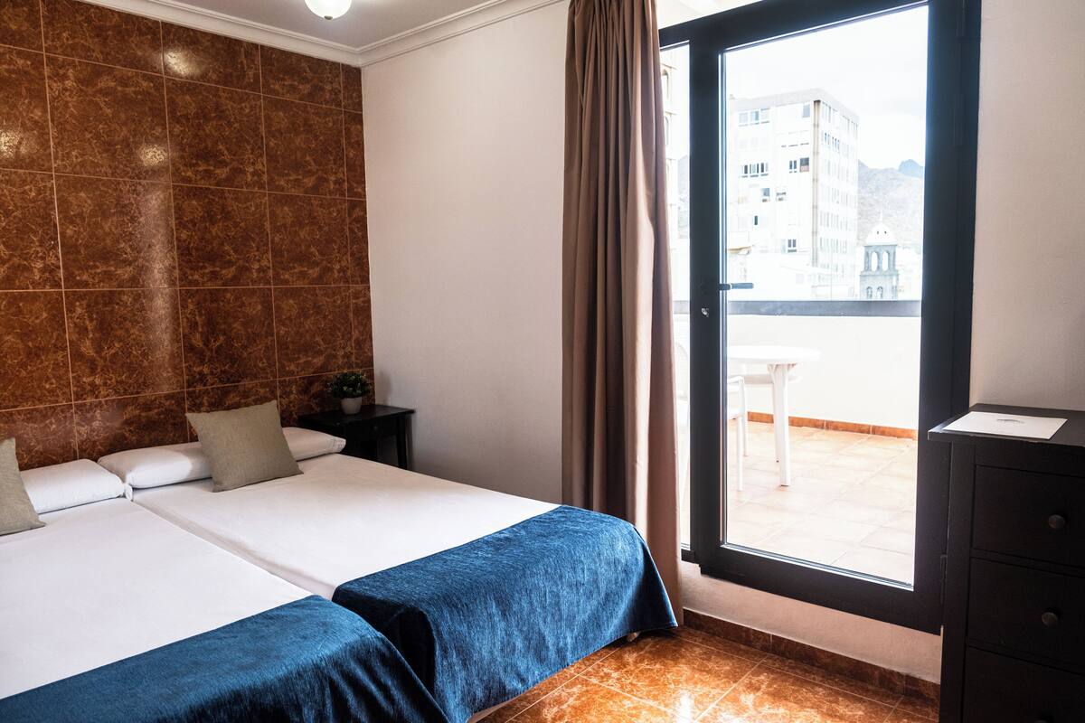 Hotellihuone, jossa on kaksi sänkyä, suuri ikkuna ja näkymä kaupunkiin.