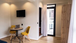 Una habitación moderna con un televisor de pantalla plana en la pared, una pequeña mesa redonda con una computadora portátil y un vaso, y dos sillas amarillas.