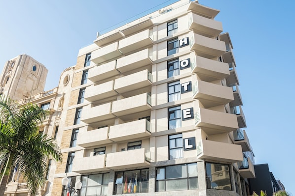 Un hôtel à plusieurs étages, doté de balcons, de grandes fenêtres et d’une enseigne bien visible indiquant « HÔTEL ».