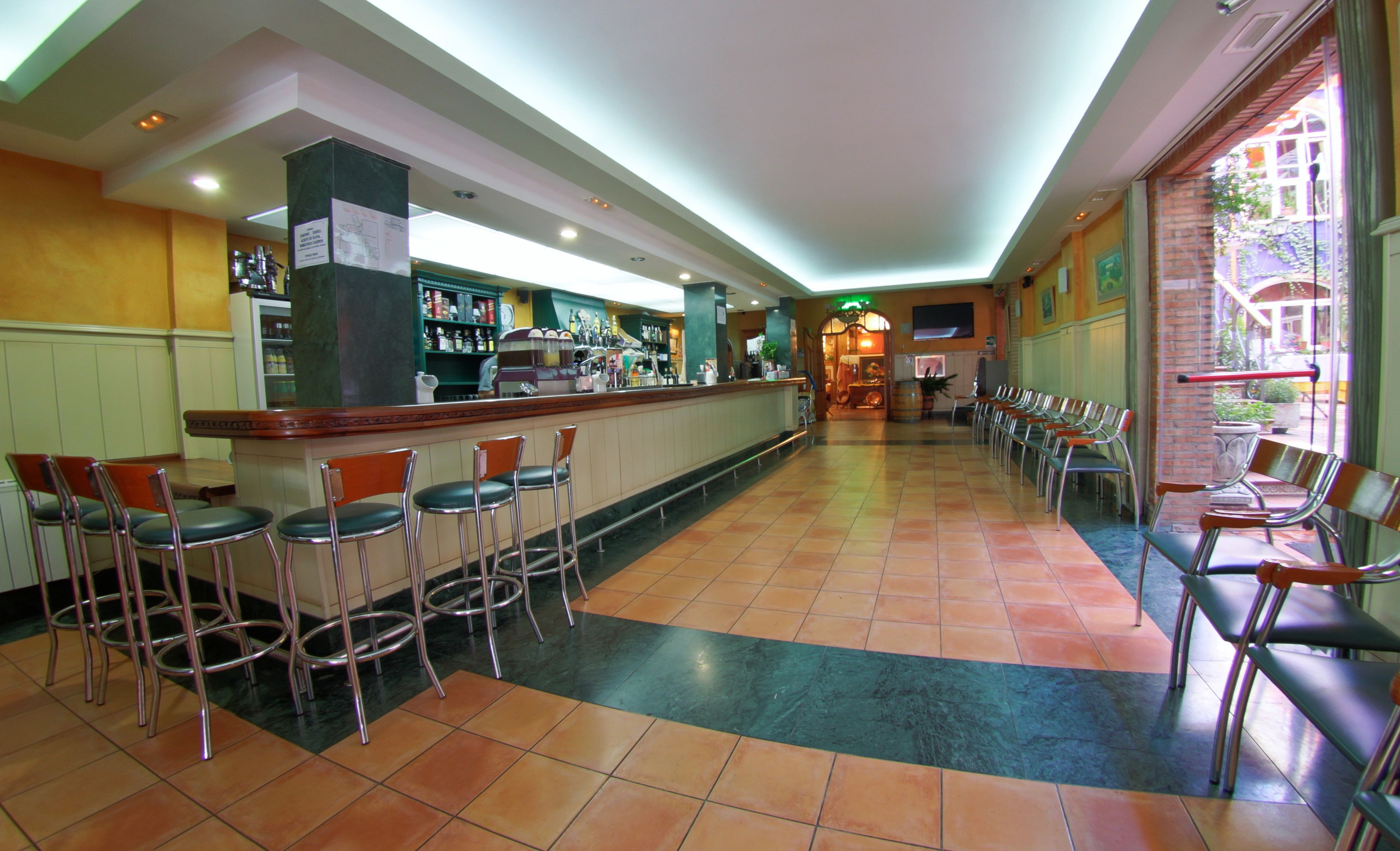 A bar area with multiple stools, a counter with a variety of bottles, and a seating area with chairs.