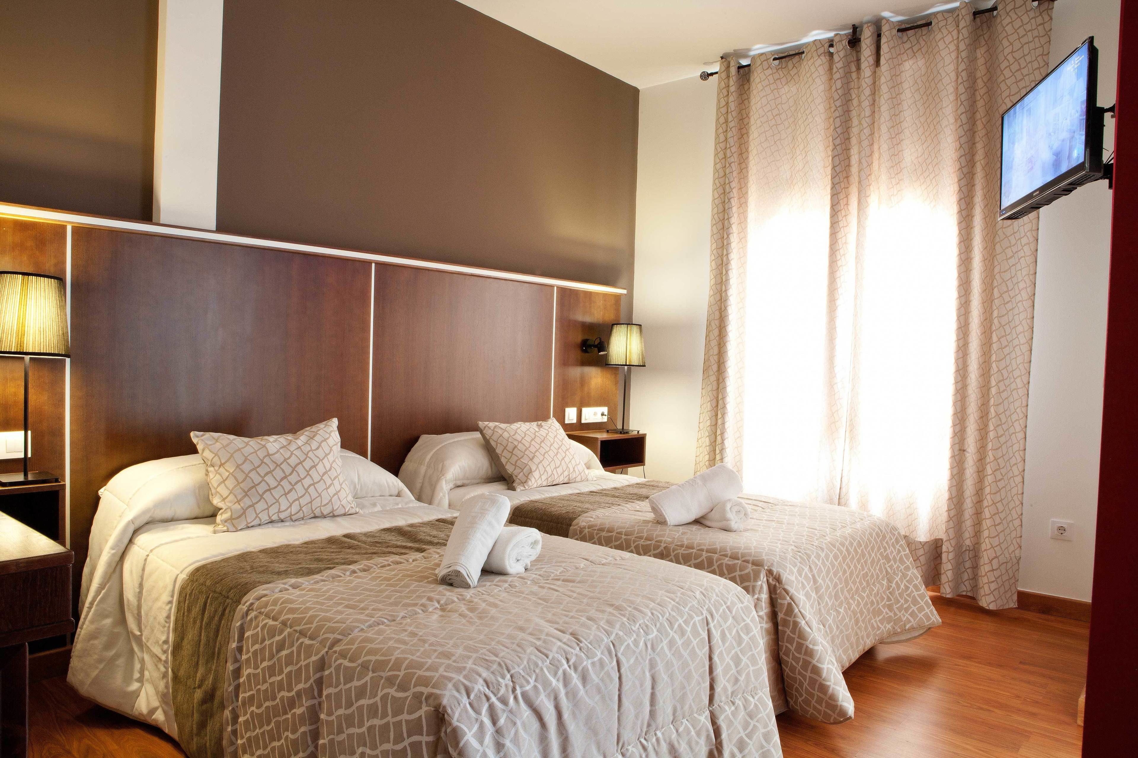Habitación de hotel con dos camas, un televisor montado en la pared y una ventana con cortinas.