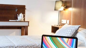 A hotel room with a bed, a nightstand, a lamp, a laptop, and a newspaper.