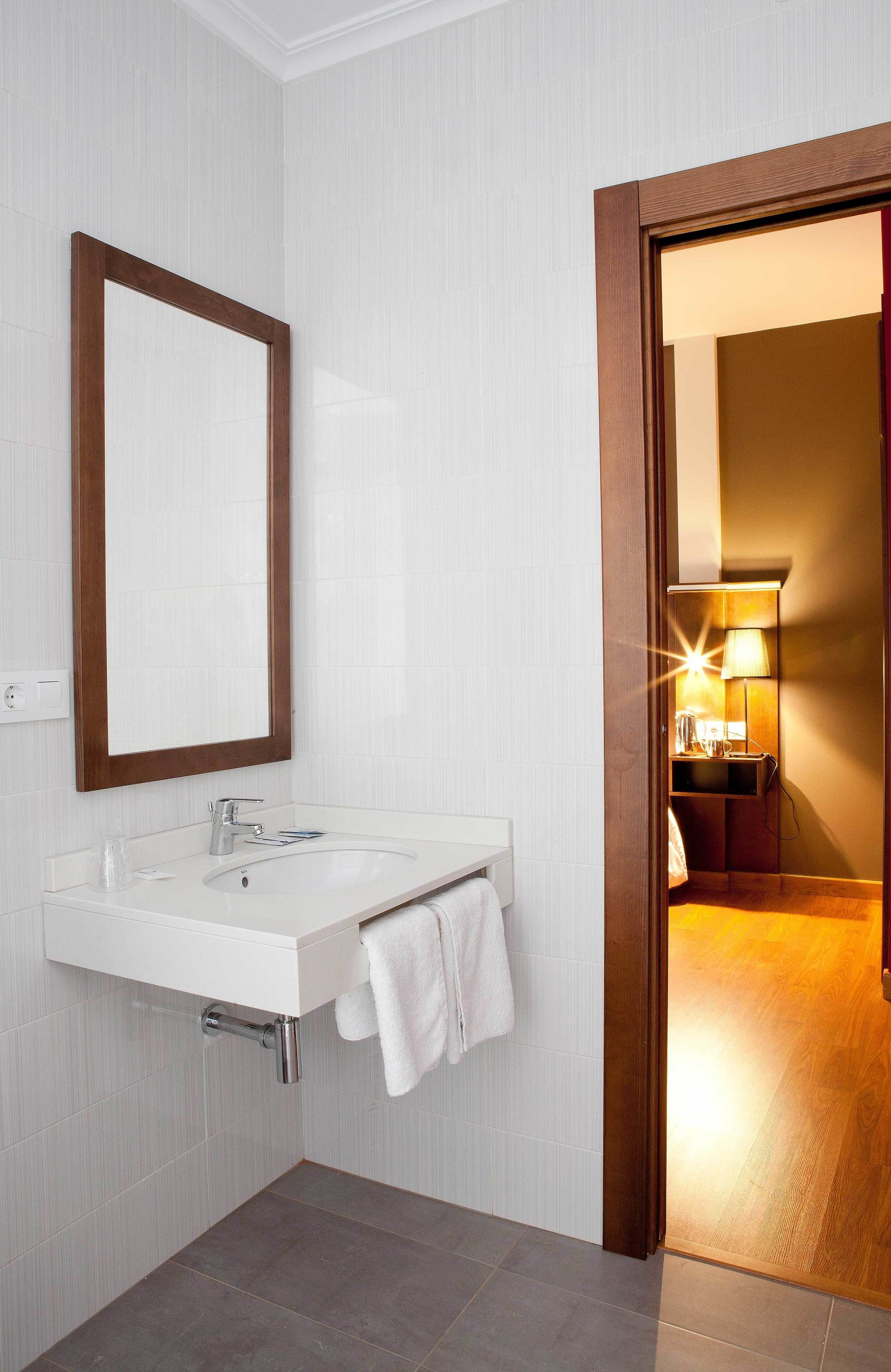 Un baño moderno con un lavamanos blanco, un espejo con marco de madera y una toalla colgada en la pared.