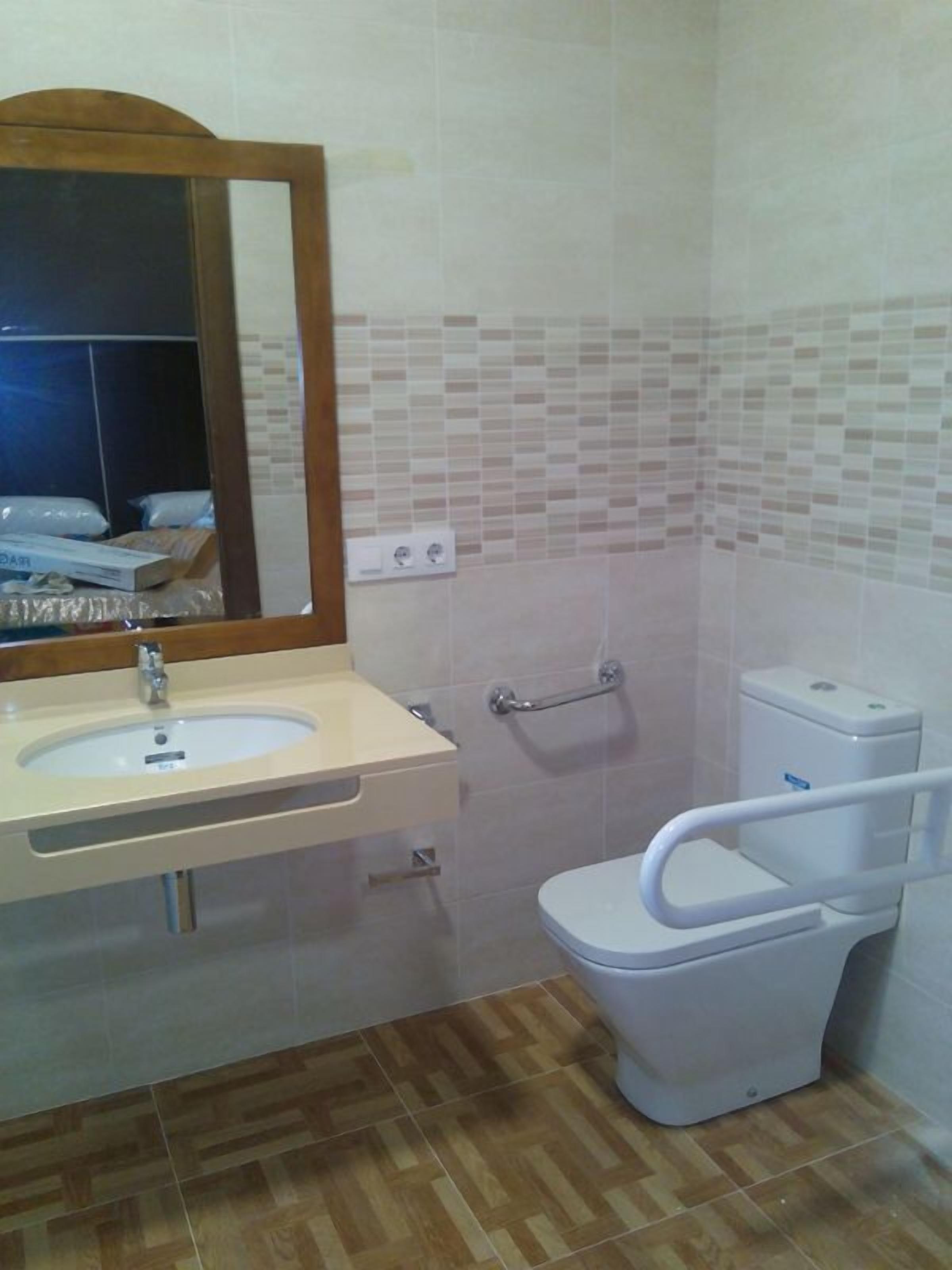 Ein Badezimmer mit Waschbecken, Spiegel, Toilette und Handlauf.