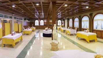 A banquet hall with tables set for dining, a central aisle, and arched windows along the walls.