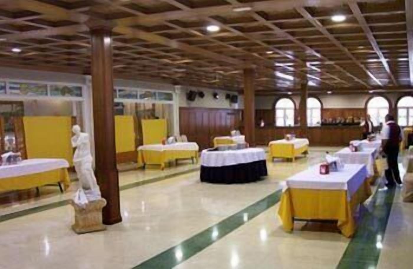 Une salle de banquet avec des tables dressées pour le repas, une statue et des lambris en bois au plafond.