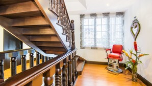A wooden staircase with a red chair and a decorative plant in a room with a large window. - Matisse Hotel (Bogotá)