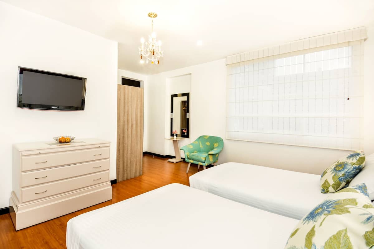 Habitación de hotel con dos camas, televisión, cómoda, silla y ventana con persianas.