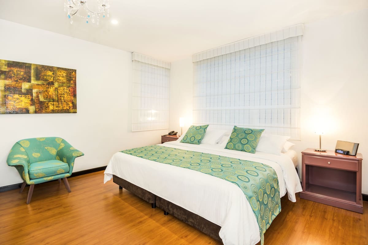 Un dormitorio con una cama grande, una silla, una mesita de noche y un cuadro en la pared.