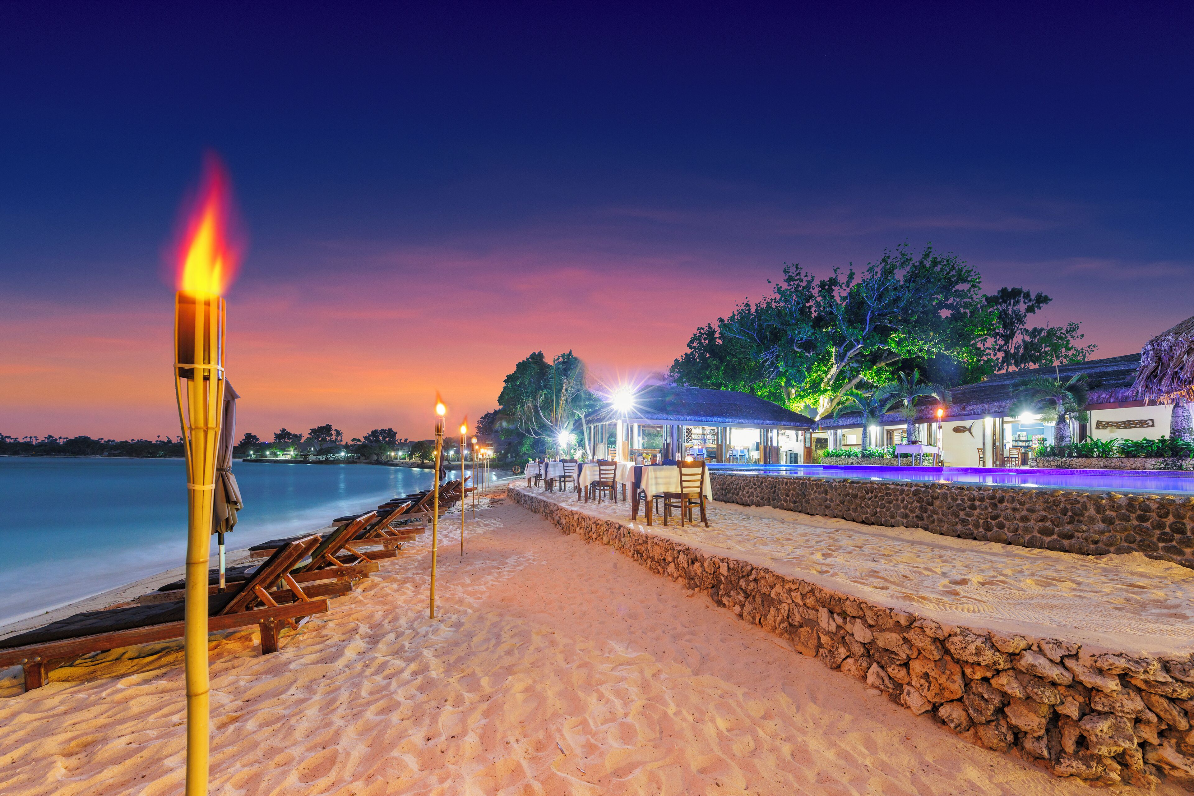 Ein Restaurant direkt am Strand mit Terrassensitzgelegenheiten, einer Steinwand und Meerblick.