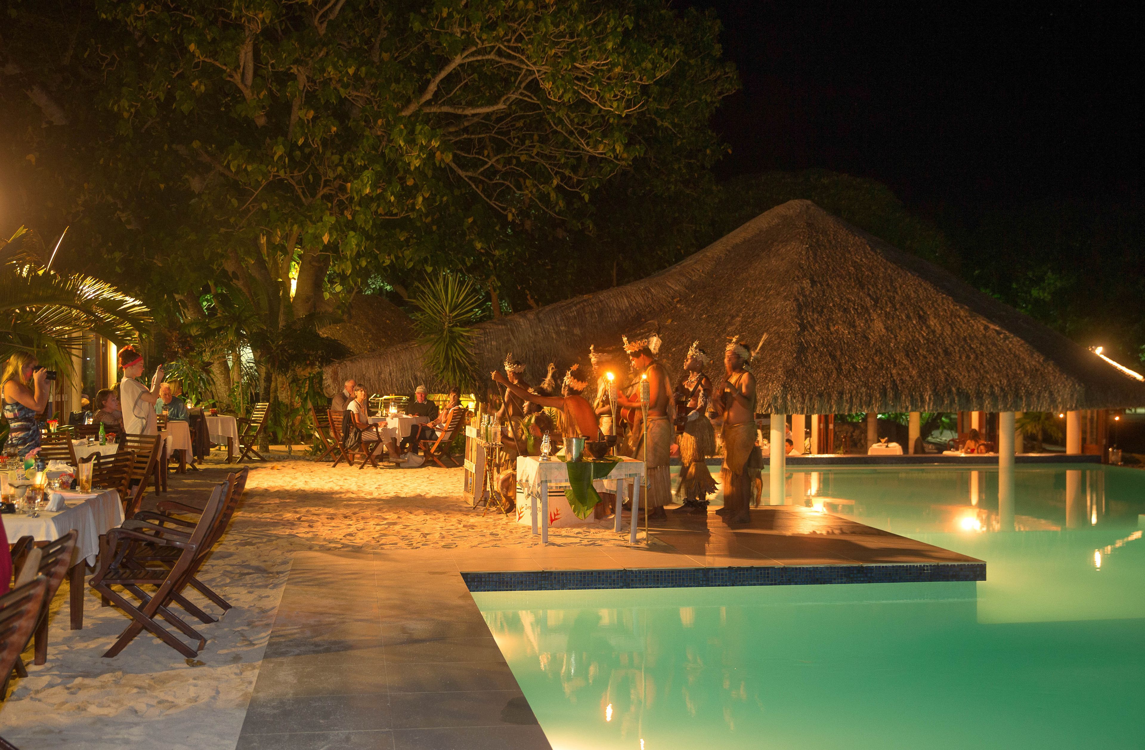 A poolside area with a thatched-roof structure, dining tables, and chairs.