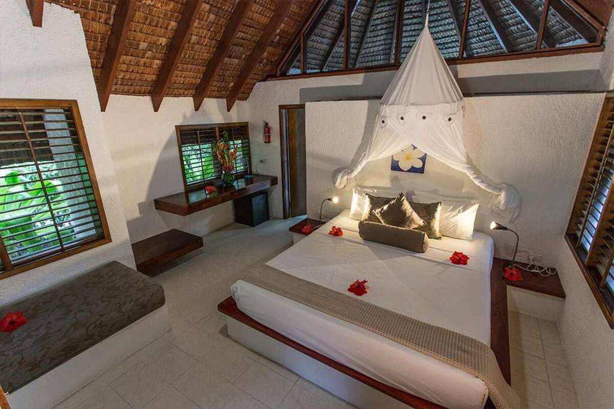 Un dormitorio con cama, dosel, banqueta, ventana y vista al cielo.