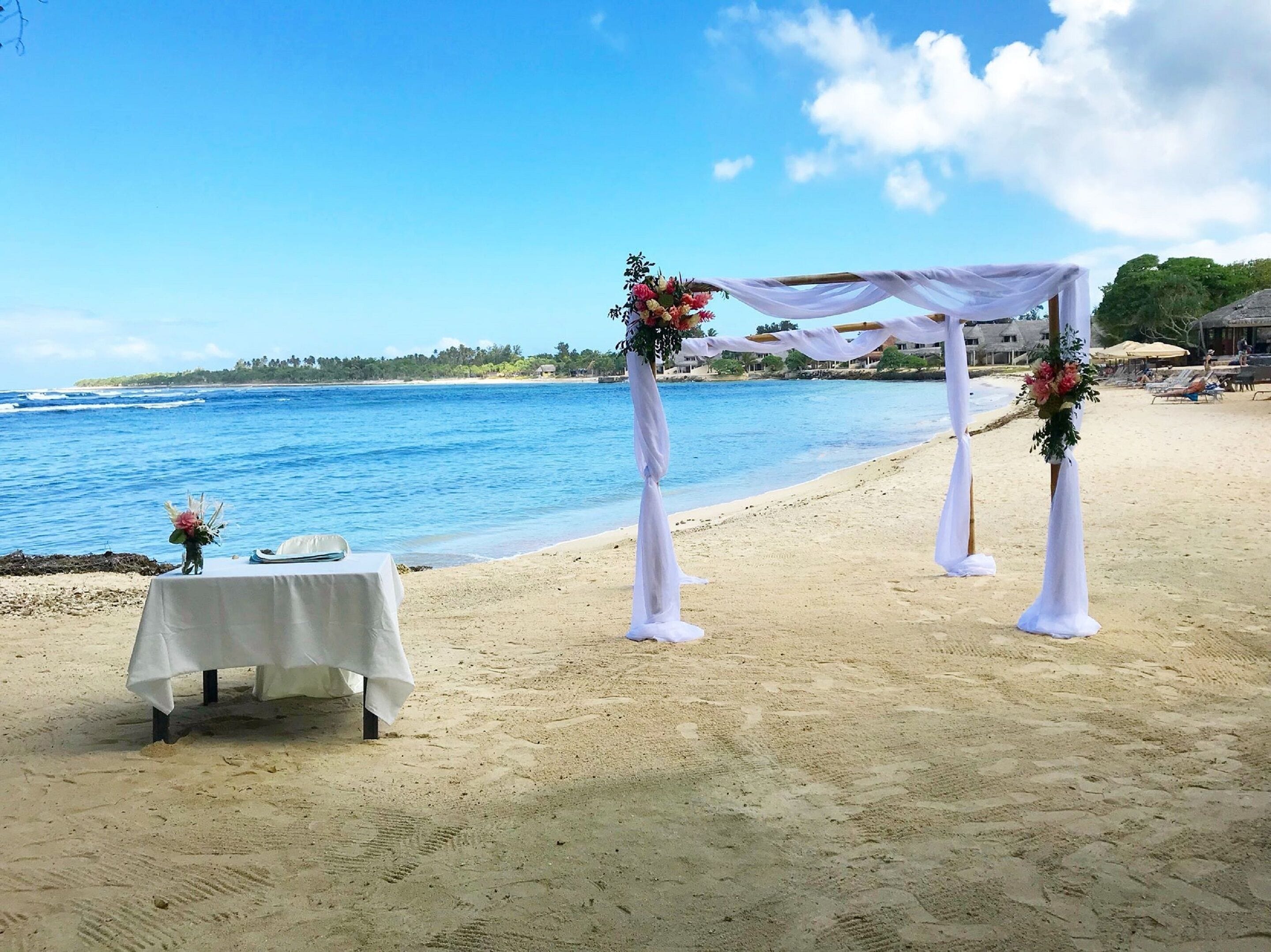 Une cérémonie de mariage organisée sur la plage, avec un dais blanc et des décorations florales.