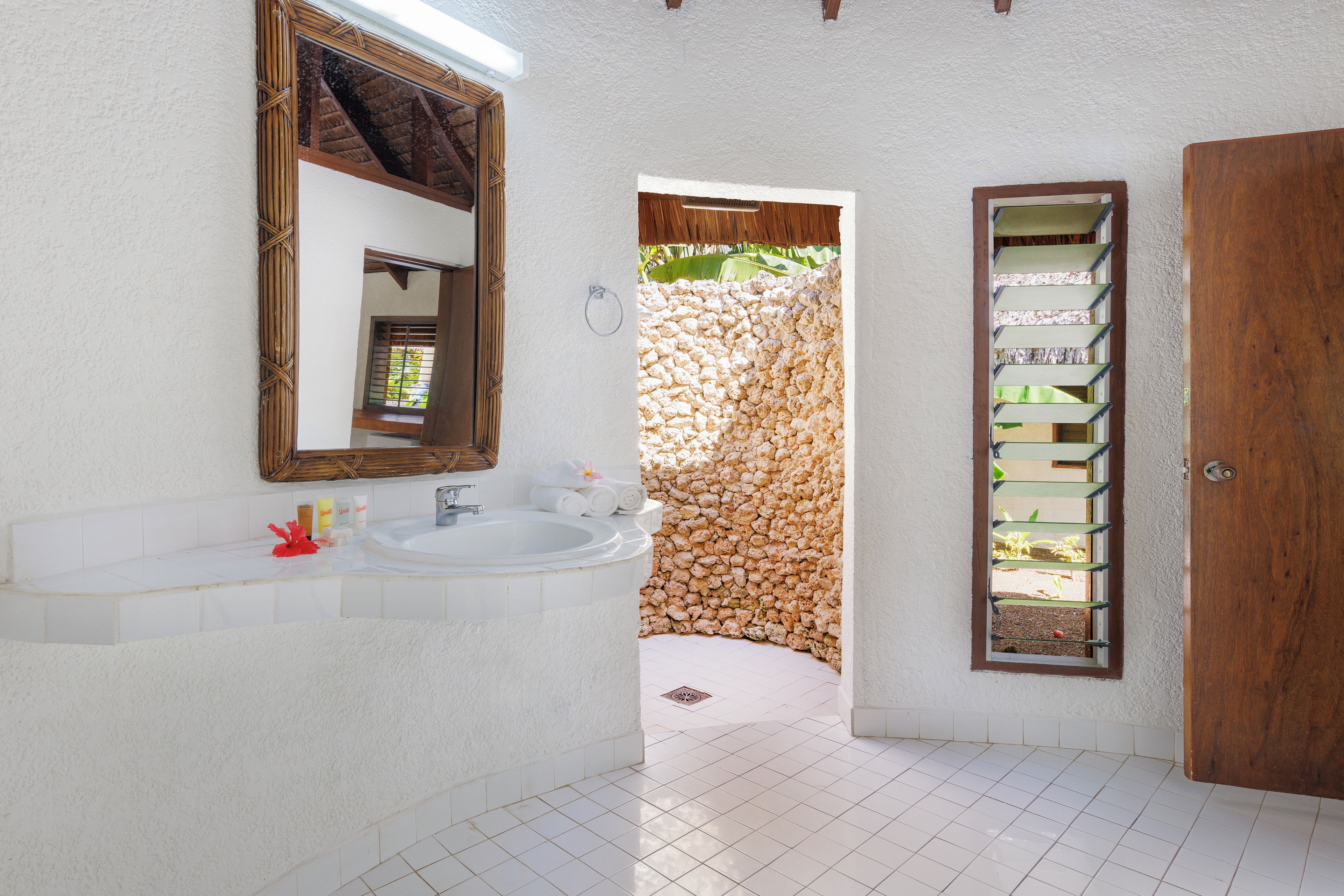 A bathroom with a white sink, a mirror, a wooden door, and a stone wall.