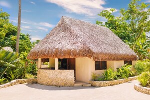 Casa con techo de paja y base de piedra, rodeada de vegetación tropical.