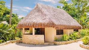 A thatched-roof house with a stone foundation, surrounded by tropical vegetation. - The Beach (Port Vila)