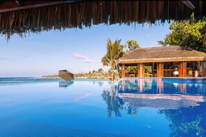 An infinity pool with a view of the ocean, a thatched-roof structure, and palm trees. - The Beach Vanuatu (Port Vila)