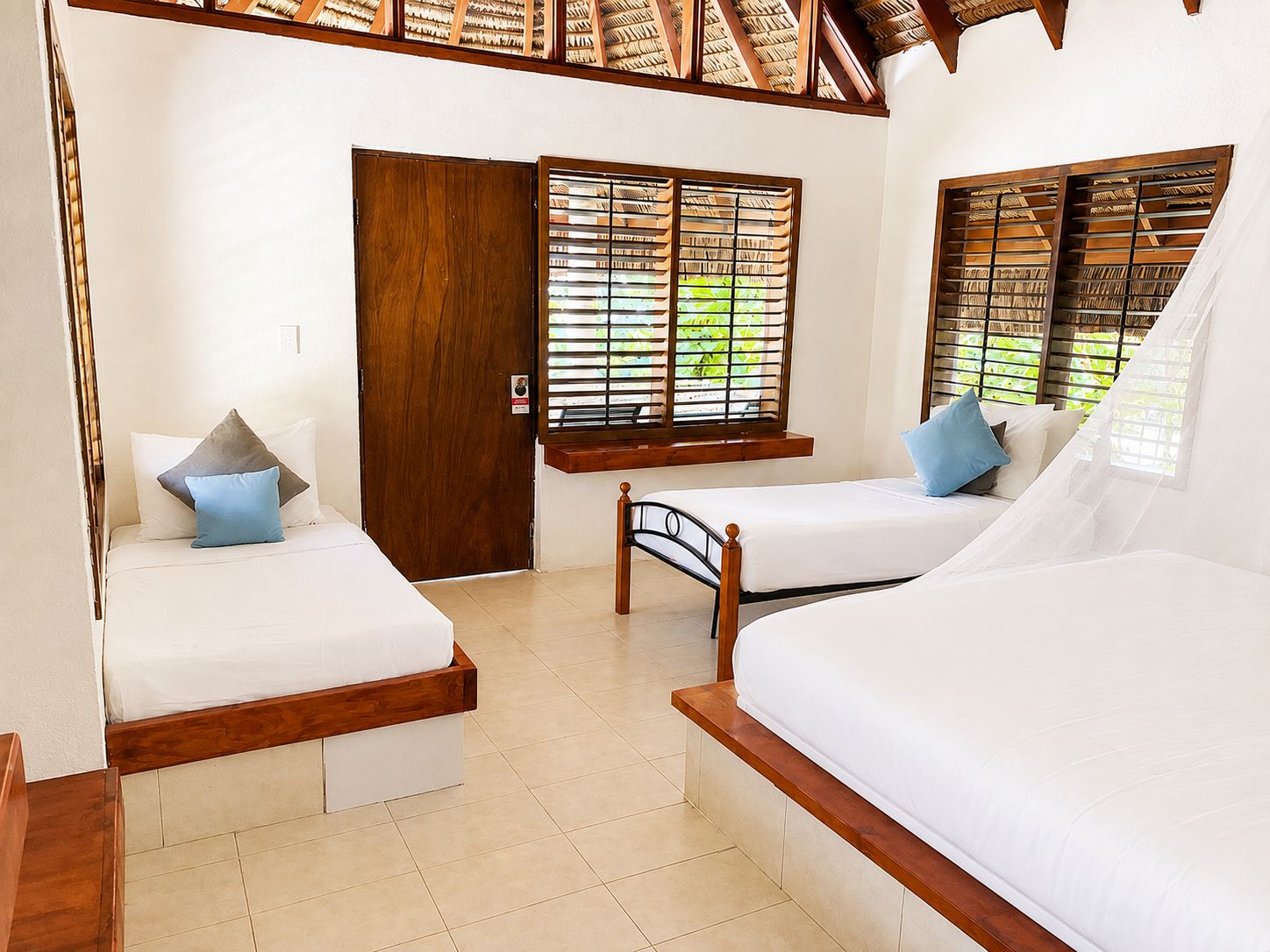 A room with two beds, a wooden door, and windows with blinds.