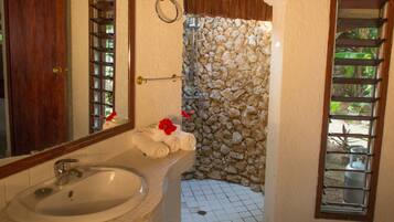 Un baño con ducha de piedra, lavamanos y espejo.