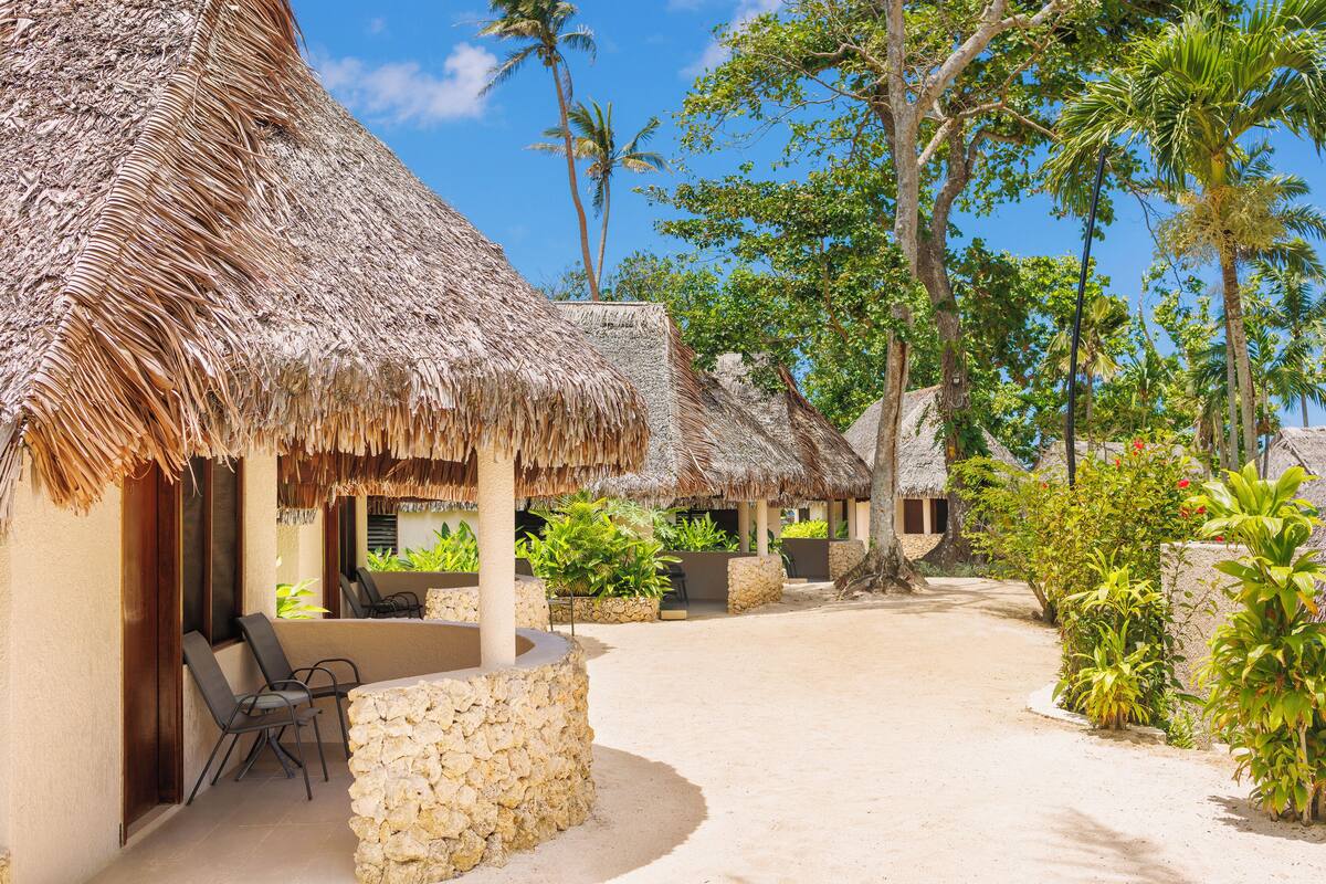 Un resort con cabañas de techo de paja, mobiliario exterior y abundante vegetación.