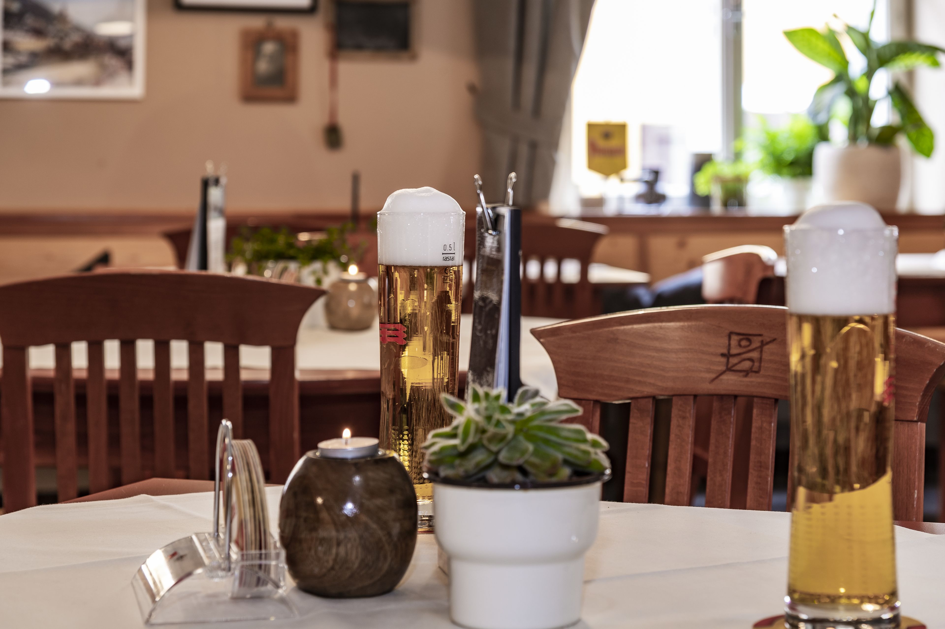 A dining table with a candle, a potted succulent, and two beer glasses.