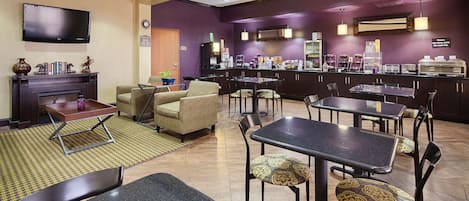 Un hall de hotel con zona de estar, chimenea, televisor, estación de café y mostrador con diferentes alimentos.