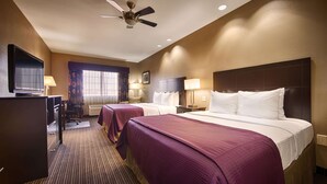 A hotel room with two beds, a desk with a television, a ceiling fan, and a window with curtains.
