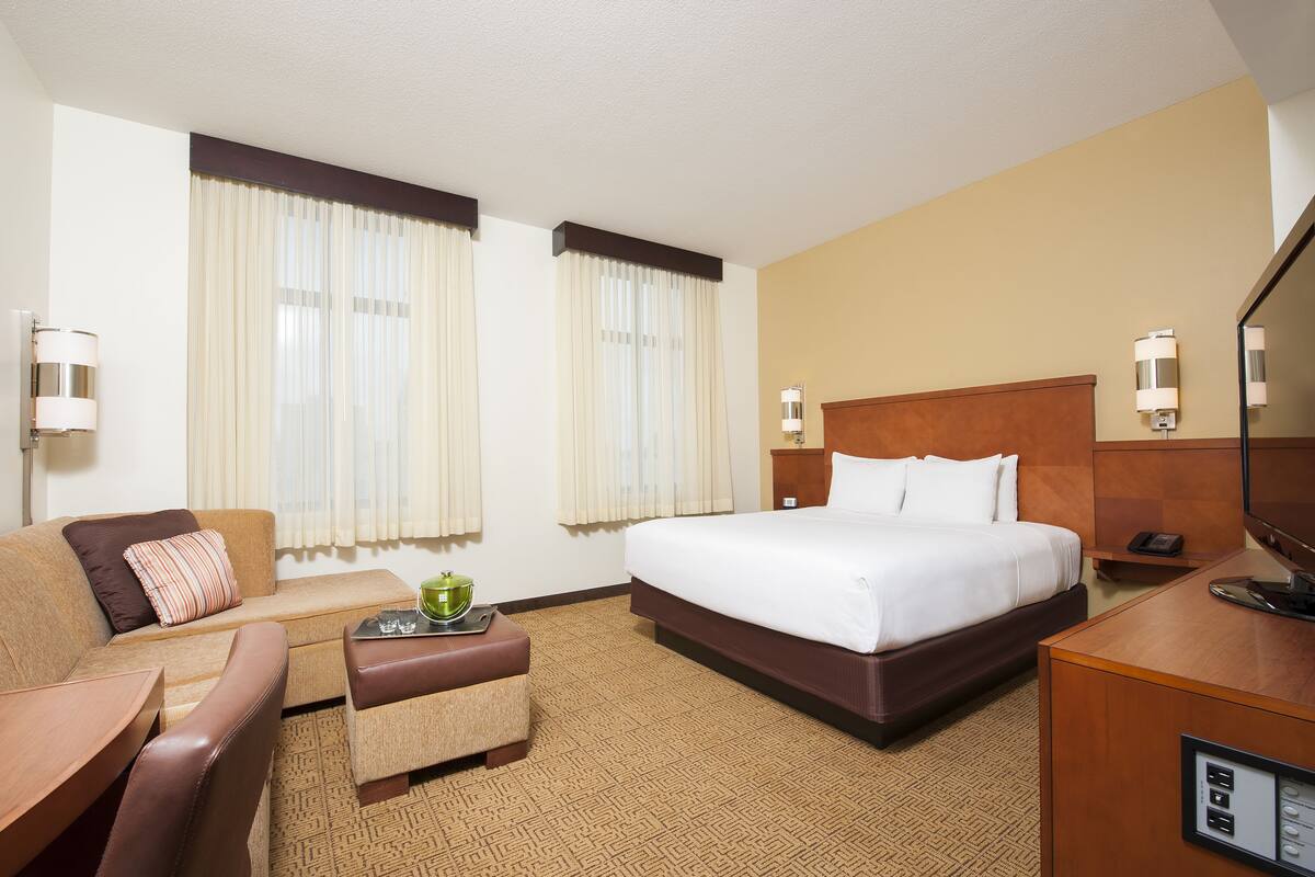 A hotel room with a bed, a sofa, a small table with a tray, and a desk with a phone and a TV.