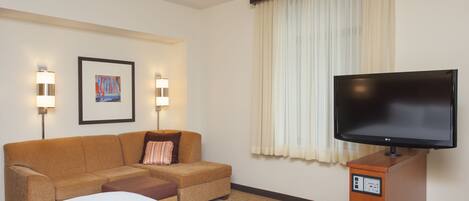 A hotel room with a bed, a sofa, a television on a wooden stand, and two wall-mounted lamps.